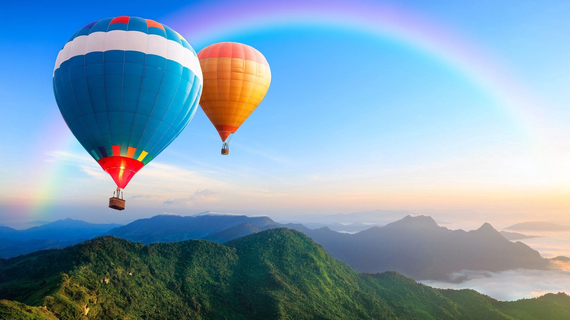 Two hot air balloons flying over a green mountain with a rainbow in the background